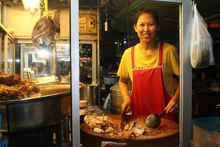 A smiling vendor at a stall of braised pork
