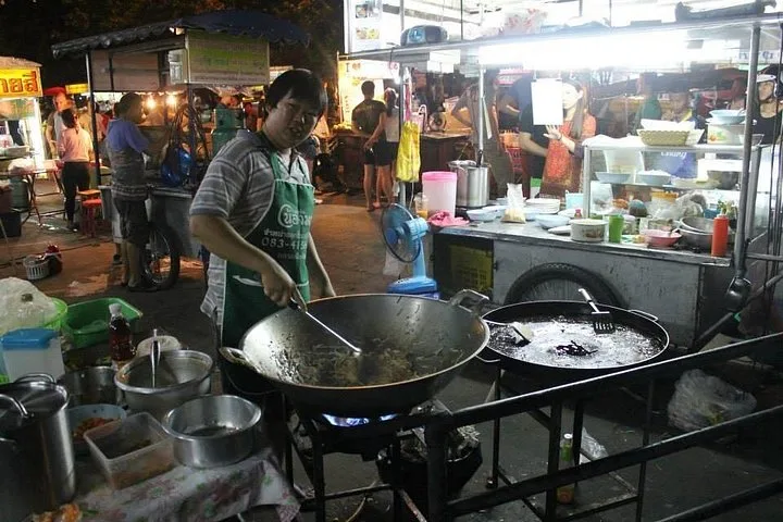 A street cook frying at a wok under a market awning